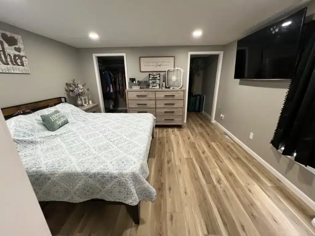 Master bedroom with light wood-look vinyl plank flooring, gray walls, dresser, wall-mounted TV, and two closets.