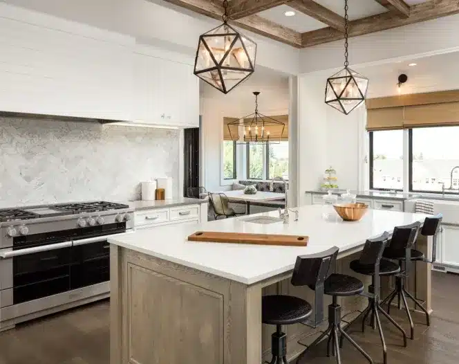 White kitchen with large island, wood bar stools, geometric pendant lights, stainless range, and herringbone marble backsplash.
