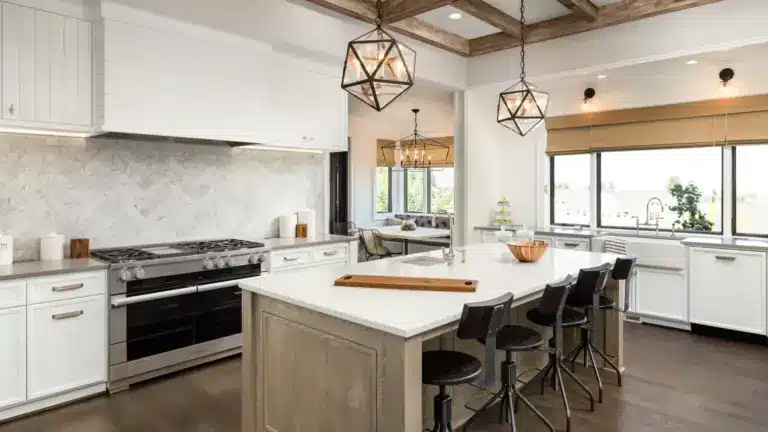White kitchen with large wood island, four black barstools, geometric pendant lights, marble backsplash, and stainless range.